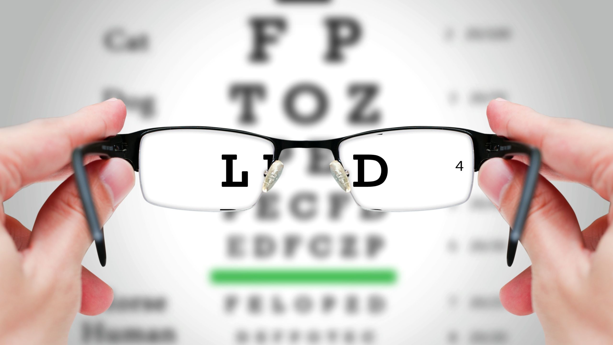 A person holds a pair of glasses up to an eye exam chart showing an L and a D