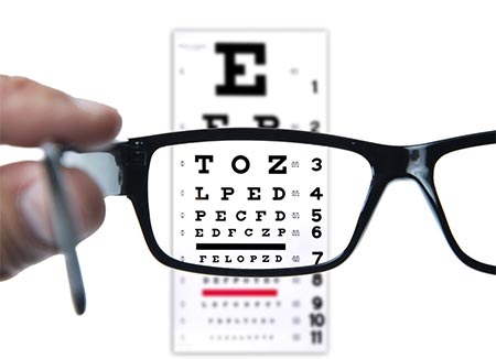 A person holding up a black pair of glasses to see an eye exam text sheet